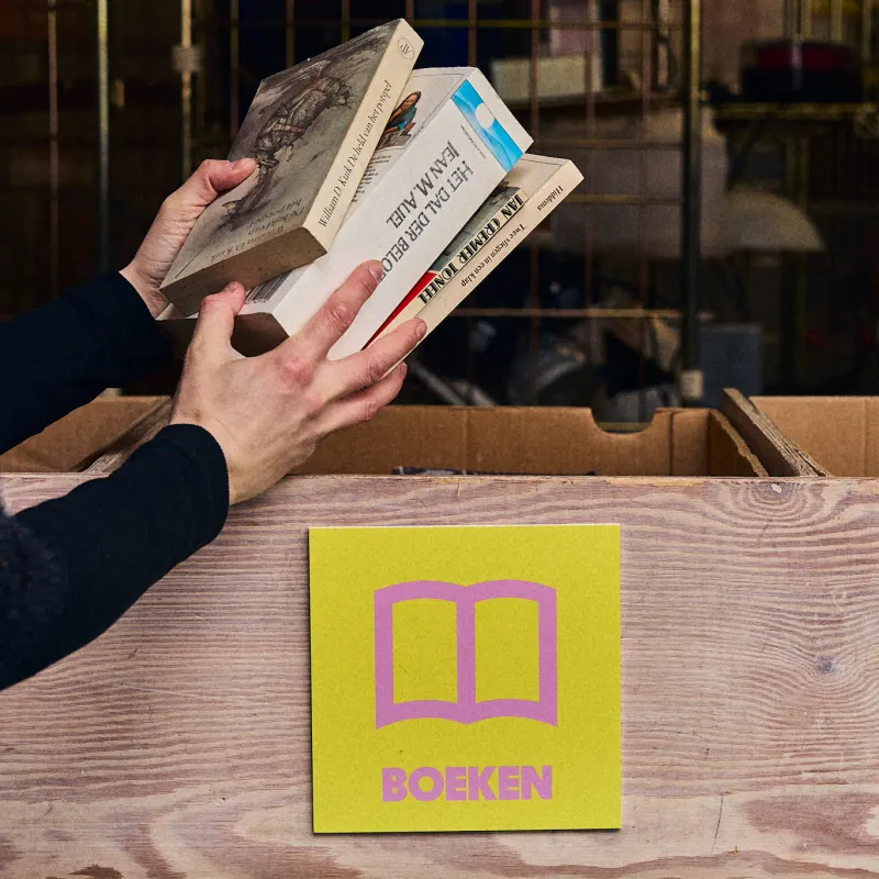 Een hand legt boeken in de bak met het label Boeken.