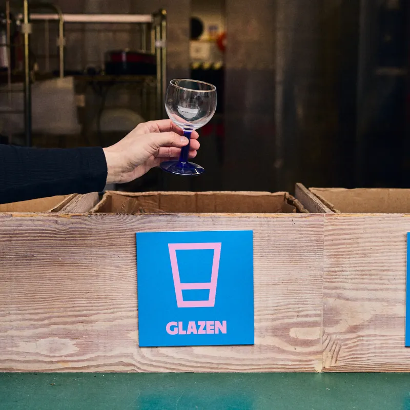 Een hand houdt een wijnglas boven de bak met het label Glazen.