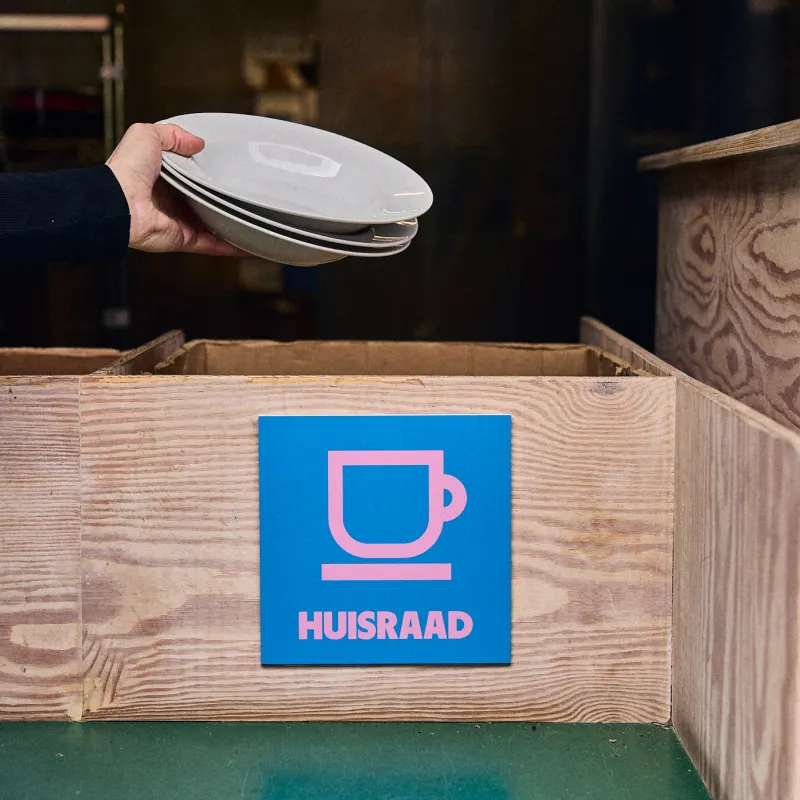 Een hand houdt borden boven de bak met het label Huisraad.