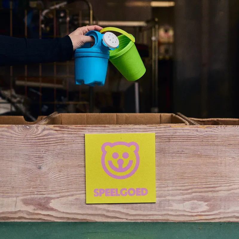 Een hand houdt speelgoedemmertjes boven de bak met het label Speelgoed.