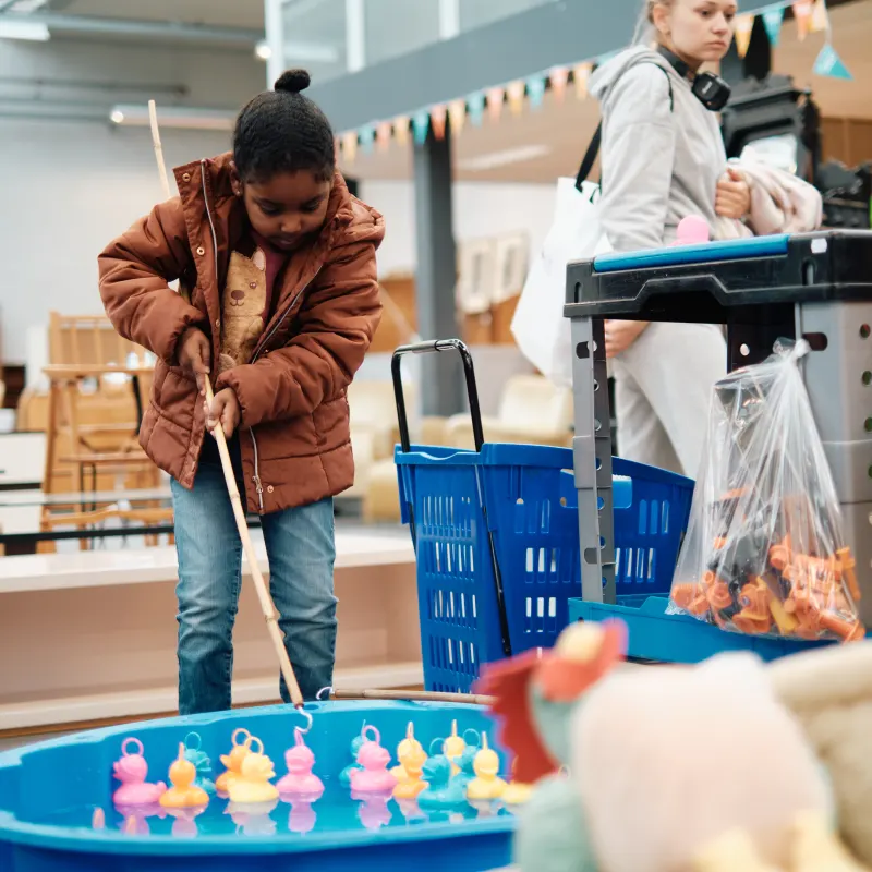 Een kind vist naar badeendjes in een blauw zwembadje in de winkel.