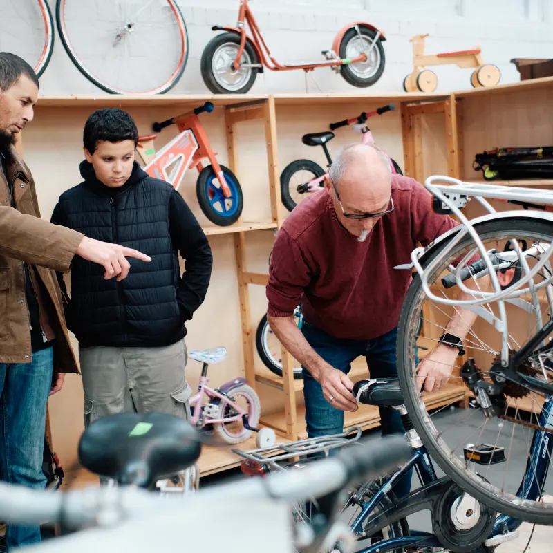 Een medewerker herstelt een fiets terwijl een jongen toekijkt.