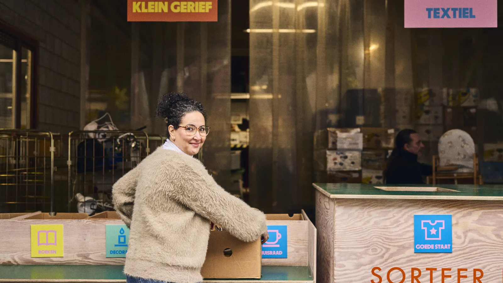 Een medewerker aan de sorteerbalie van een geefpunt kijkt lachend op.