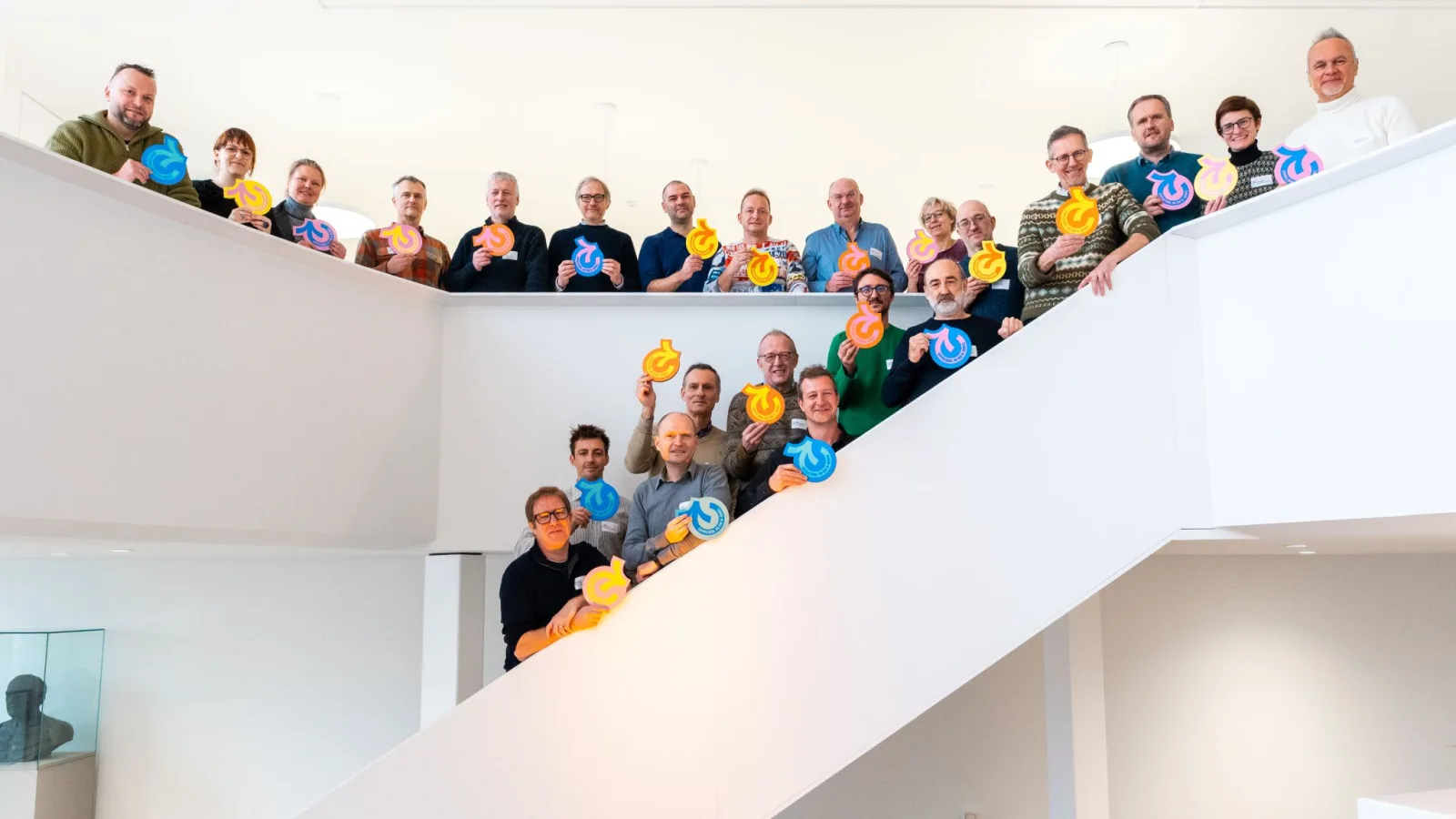 Medewerkers met het Kringwinkel-logo in de hand bij de oprichting van Kringwinkel Groep